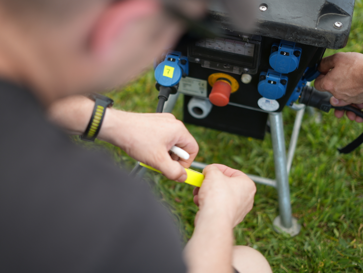 Technicien électricité repérant les arrivées d'une armoire 32A pour un événement extérieur.